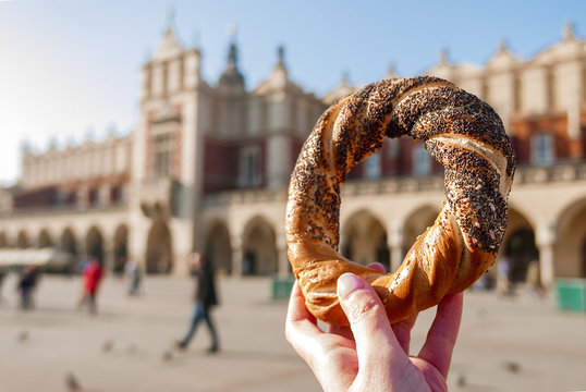 Woman holding bagel / obwarzanek / pretzel - traditional Polish snack on Market Square in Cracow. .Tourist hand holding pretzel on the Cracow Cloth Hall background.