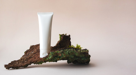 White plastic tube with facial moisturizer cream or facial cleanser on tree bark on beige background with copy space. Concept bio organic beauty products with natural extract and vitamin - obrazy, fototapety, plakaty