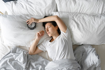 View from above. The girl sleeps next to the alarm clock. Trying to turn off the ringing alarm...