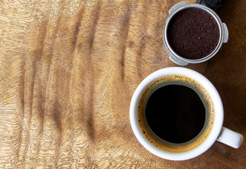 Top view of a cup of coffee and ground coffee on a brown wooden table.