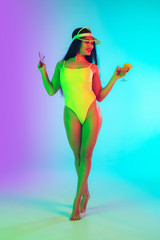 Cocktail. Beautiful young girl' portrait isolated on gradient studio background in neon light. Woman in fashionable bodysuit. Facial expression, summer, weekend, beauty, resort concept. Vacations.