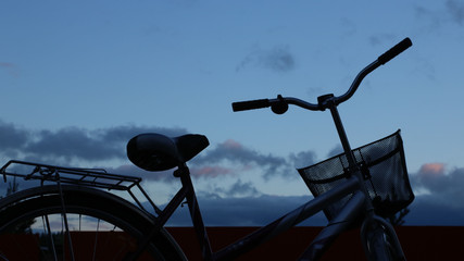 silhouette of the top of a walking bike with a basket against the sunset sky in the evening twilight