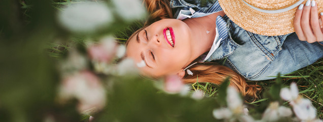 Panoramic banner of young cheerful carefree hippie woman lay on green grass and smile on...