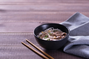 Asian cuisine, Vietnamese pho bo soup in a black plate on a wooden background