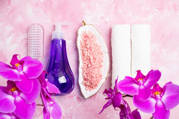 Fototapeta na wymiar Spa treatment concept. Natural spa cosmetics products, sea salt, massage brush, tropic flowers on pink background. Spa background flat lay. Top view