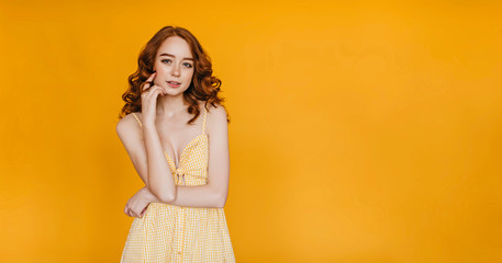 Slim beautiful girl with ginger hair posing on yellow background. Studio portrait of caucasian cute woman expressing interest.