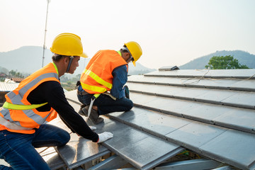 Roofer worker in special protective workwear and gloves installing new roof under construction...