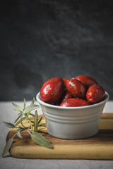 Red olives in a rustic dish with rosemary sprig.