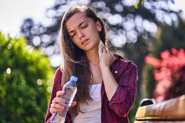 Tired sweating woman with refreshing water bottle wipes her neck with a napkin during walking in a...