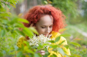 red haired pretty girl with closed eyes posing with bouquet of white flowers in yellow sweater on forest background
