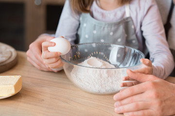 Little girl cracking egg to bowl, helping father with cooking pastry