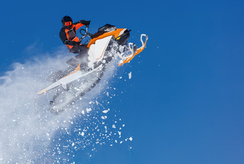 Extreme sport race snowmobiles. Snowmobile in high jump above track. Sportsman on snowmobile. Winter competition, sunny day. Trick against blue sky. Snow motor sports Copy space.