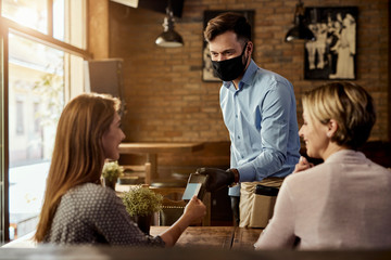 Guests making contactless payment to a waiter in a cafe.