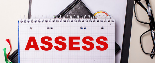 The word assess written on a white paper on a light background next to glasses