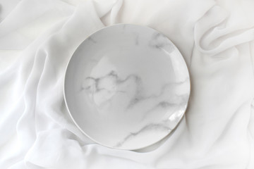 Empty marble plate  on white silk background. Elegant minimalist wedding table setting. Top view.