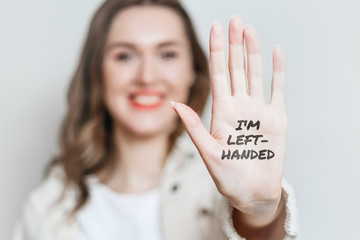 Left-handed girl shows her left hand to the camera and smiles isolated over gray background, celebrating left-handed day, text I'm left-handed on hand