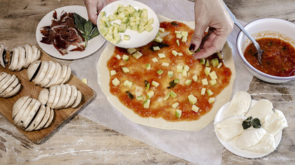 Cook hands making pizza dough and preparing with tomato, mushrooms, ham, mozzarella and parmesan cheese.