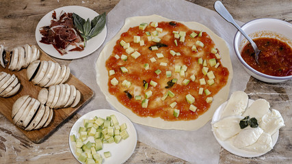 Cook hands making pizza dough and preparing with tomato, mushrooms, ham, mozzarella and parmesan cheese.