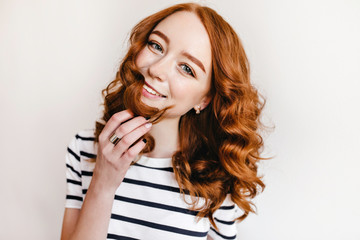Joyful lady wears earrings and ring smiling to camera. Carefree ginger female model posing on white background and laughing.