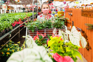 Young girl wearing a face mask while pushing a cart in a greenshouse full of plants