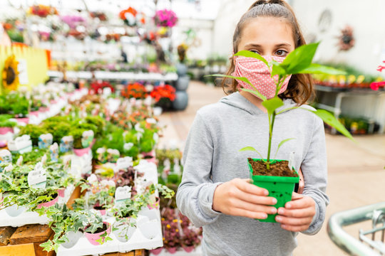 Young girl wearing a face mask while holding a plant in a greenhouse - Powered by Adobe