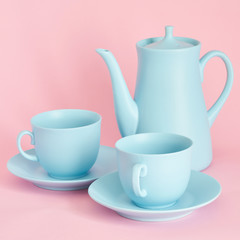 minimalism concept with light pastel colored blue cups teapot and plate on pink background.