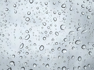 Big raindrops on a transparent glass against a cloudy blue sky. Condensation and precipitation concept.