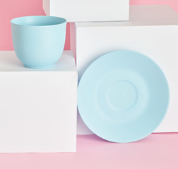 minimalism concept with light pastel colored blue cups and plate with white paper cubs on pink background.