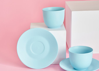 minimalism concept with light pastel colored blue cups and plate with white paper cubs on pink background.