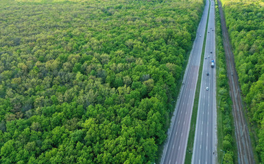 Aerial view of a highway through a bright green forest. Straight road through the forest