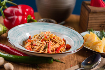 Pasta with tomatoes and peppers, and parmesan cheese in a blue plate on a wooden table