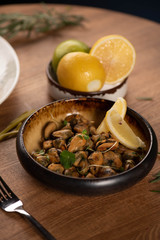 stewed mussels with microgreens and lemon in a black deep plate on a wooden table