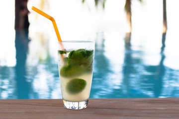 Glass of iced mojito cocktail at the edge of swimming pool. Outdoor pool background with copy space.