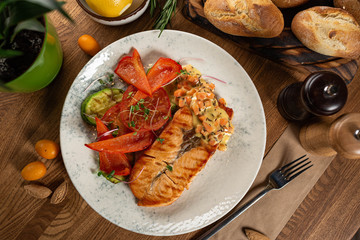 grilled salmon steak with red pepper and zucchini with cream sauce on a wooden table. top view. 