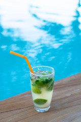 Glass of iced mojito cocktail at the edge of swimming pool. Outdoor pool background with copy space.