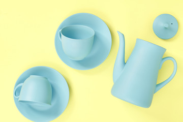 minimalism concept with light pastel colored blue teapot, plates and cups on yellow background.  Flat lay. Tea time concept. Empty space