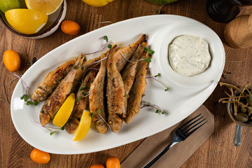 fried red mullet with white sauce and micro-greens on a wooden table. top view