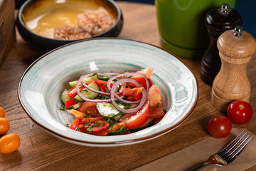 tomato and cucumber salad with red onion and herbs in a round blue plate on a wooden table