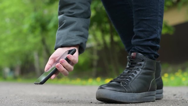 The girl finds a smartphone on the street and picks it up from the asphalt. Close-up, no face