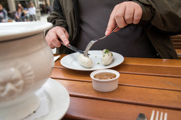 Mann isst Münchener Weißwurst mit Messer und Gabel, süßen Senf und Brezel und löst Wurst richtig aus Pelle draußen in Biergraten