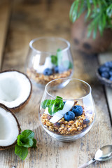 A glass of healthy breakfast: granola with fresh blueberries, coconut chips and mint. Vertical