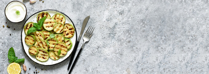 Grilled zucchini with sauce on concrete background. View from above.