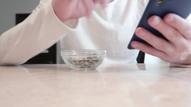 A young man uses a smartphone during break. Pumpkin seeds in a transparent bowl