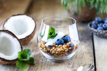 A glass of healthy breakfast: granola with fresh blueberries, coconut chips and mint. Vertical