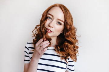 Graceful blue-eyed girl posing on light background with interested face expression. Studio shot of ginger cute woman playing with her hair.