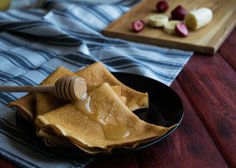 Several pancakes on a black plate, sprinkled with honey. Wooden background, side view, horizontal orientation.