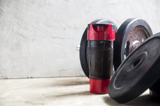 iron Dumbbell and whey protein shaker.  Fitness or bodybuilding concept background. Product photograph on grey, concrete floor