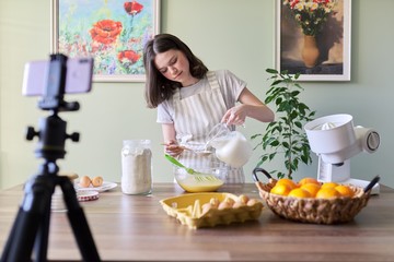 Obraz na płótnie Canvas Girl teenager young food blogger cooking orange pancakes, pours milk