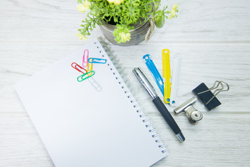 Workspace with office supplies, pen, green leaf, and paper on wooden background. Flat lay, top view office table desk. Copyspace and selective focus.