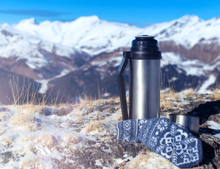 Hiking still life with a metal thermos on top of a mountain and in the background